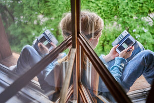 Ein Junge sitzt am Fenster und schaut auf sein Handy