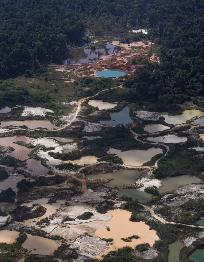 Von oben blickt man auf eine zerfurchte tropische Landschaft, bestehnd aus mit schlammigen Wasser gefüllten natürlichen Becken und Sandpisten, die sich zwischen ihnen schlängeln