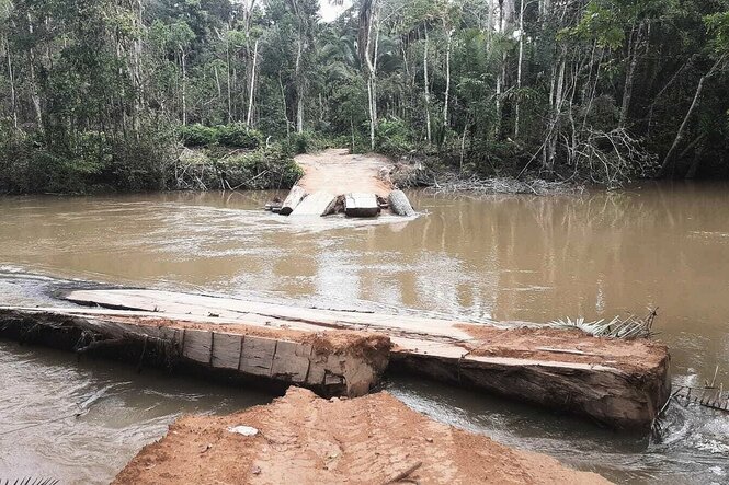 Fluss mit schlammigen Wasser, an dessen beiden Enden Baumstämme einer ehmaligen Brücke liegen