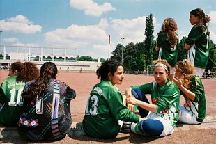 Junge Fußballerinnen sitzen am Rand eines Spielfelds.
