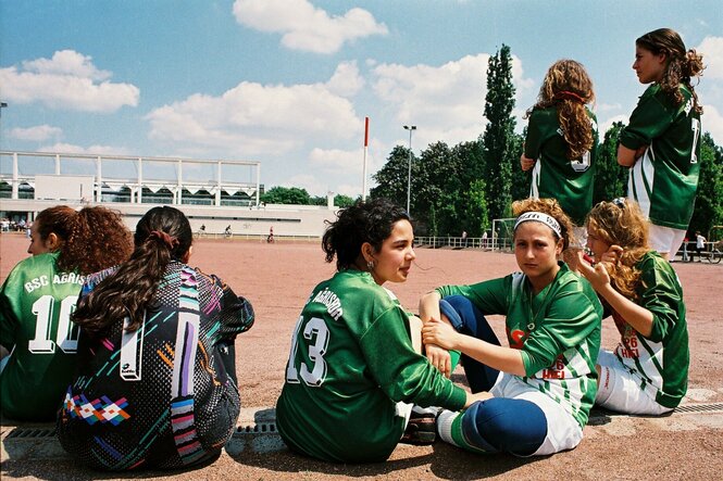 Junge Fußballerinnen sitzen am Rand eines Spielfelds.