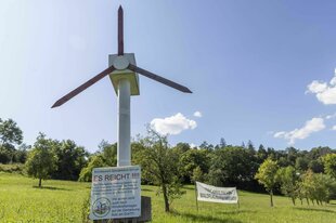 Protest gegen Windkraftanlagen: auf einer Wiese vor mit Bäumchen steht ein selbt gebasteltes Windrad, am Fußende ist ein Schild angebracht: Es reicht !!!