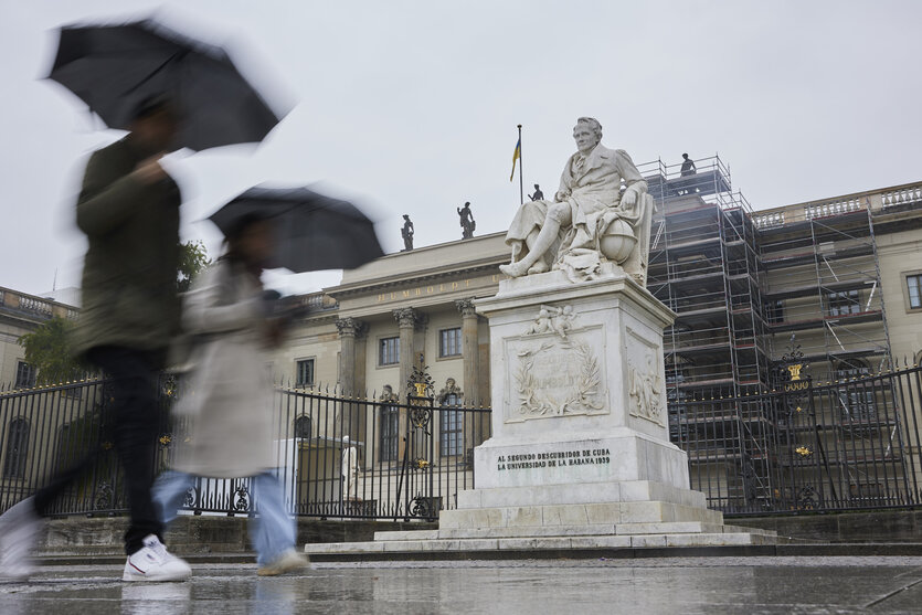 Zwei Menschen mit Regenschirmen laufen am Hauptgebäude der Humboldt-Universität zu Berlin vorbei