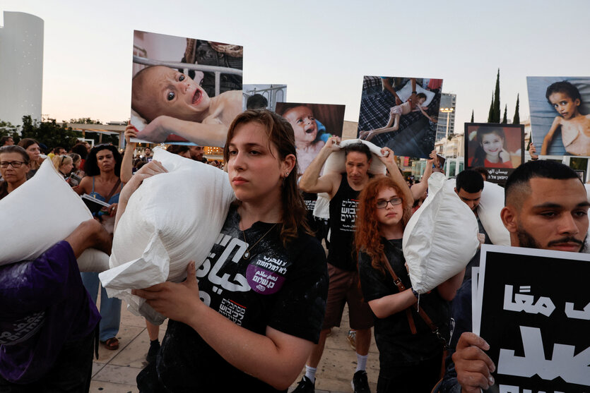 Demostrant*innen in Tel Aviv tragen Mehlsäcke und Bilder von hungernden Kindern