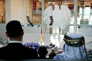 Zwei Jesid*innen sind auf der Besuchertribüne des Bundestages zu sehen, im Vordergrund der Bundesadler im Plenarsaal