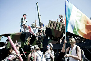 Menschen mit schminke auf dem Gesicht und roten Nasen lachen und halten eine Regenbogenflagge