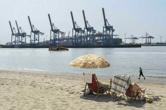 Zwei Personen sitzen in Hamburg am Elbestrand und schauen auf den Hamburger Hafen
