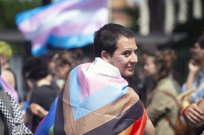 Eine in eine Pride-Flagge gehüllte Person auf einer Demonstration dreht sich zum Betrachter