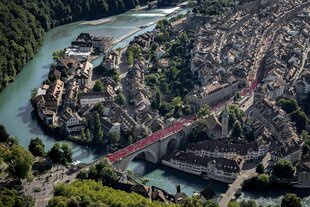 Eine Luftaufnahme zeigt die Stadt Bern von oben. Schweizer Fußballfans laufen über eine Brücke