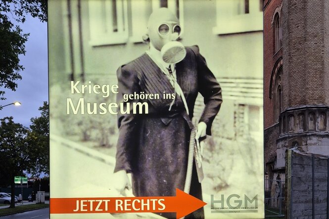 Plakat mit einer Frau mit Gasmaske und Aufschrift: "Krieg gehört ins Museum"
