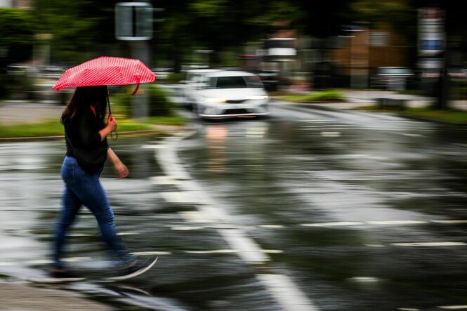 Eine Frau mit einem Regenschirm überquert im Regen eine Straße.