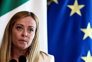 Giorgia Meloni hat glatte blonde Haare und schaut ernst