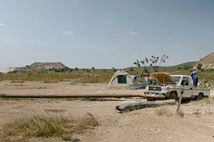 Ein AVZ-Mitarbeiter pumpt Diesel in einen Generator, der Wasser aus dem altern "Roche Dure" Tagebau ableitet. Die Berge im Hintergrund sind 'Tailings Dumps' aus früheren Bergbauaktivitäten. Tantalex hofft, die Tailings Dumps in naher Zukunft zur Gewinnung von Lithium abbauen zu können.