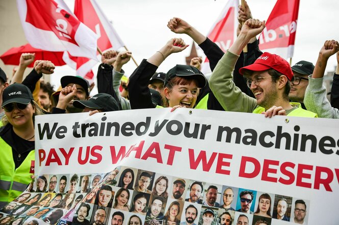 Menschen protestieren mit hochgestreckten Fäusten, Banner und Verdi-Fahnen