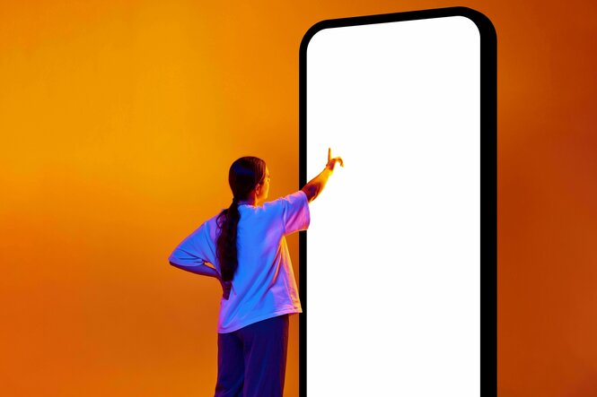 Eine Person zeigt auf das Display eines überrgroßen Handys