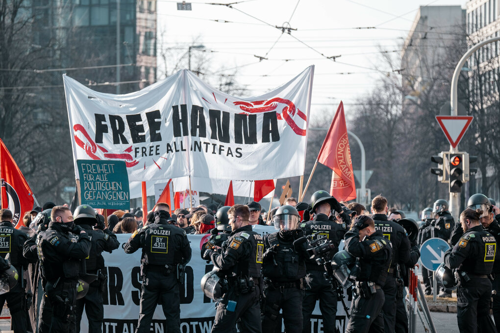 Demonstrierende halten ein Banner in die Höhe, auf dem steht:"FREE HANNA". Mehrere Polizisten sichern die Demonstration