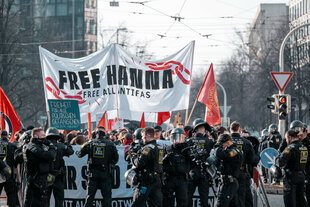 Demonstrierende halten ein Banner in die Höhe, auf dem steht:"FREE HANNA". Mehrere Polizisten sichern die Demonstration