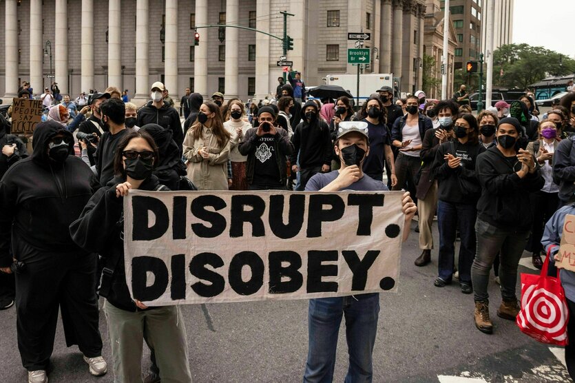 Menschen stehen vor einem Gebäude in New York, zwei halten ein Schild mit dem Schriftzug "Disrupt, Disobey"