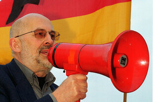 Horst Mahler mit einem Megafon vor einer Deutschlandfahne.
