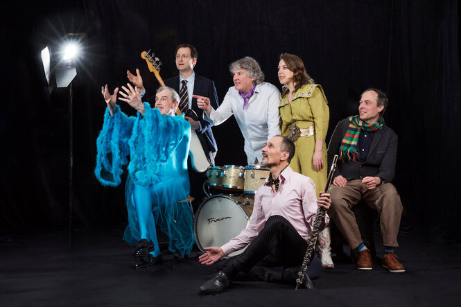 Man sieht: die Band Jacques Palminger & 440 Hertz in Kostümen und mit Instrumenten wie: Schlagzeug, Bass-Gitarre und Klarinette