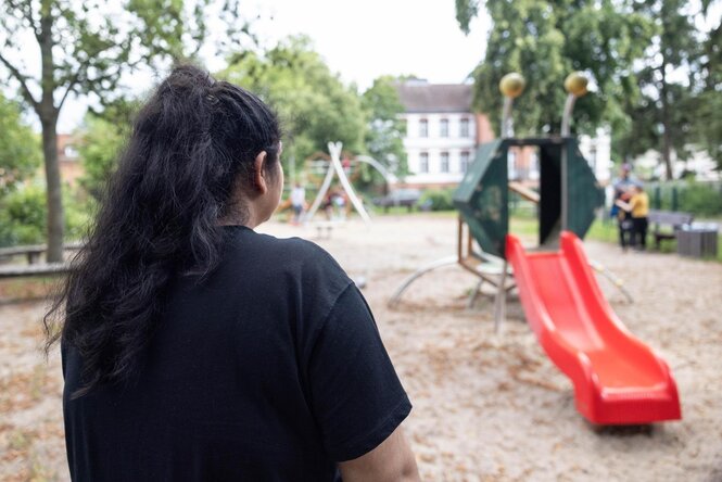 Eine Frau mit schwarzem T-Shirt schaut auf einen Spielplatz