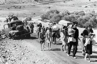 Schwarz-Weiß-Foto: Menschen mit einem Esel gehen eine Straße entlang in einer dürren, staubigen Landschaft