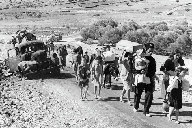 Schwarz-Weiß-Foto: Menschen mit einem Esel gehen eine Straße entlang in einer dürren, staubigen Landschaft