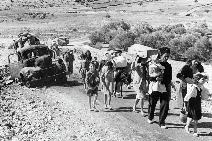 Schwarz-Weiß-Foto: Menschen mit einem Esel gehen eine Straße entlang in einer dürren, staubigen Landschaft