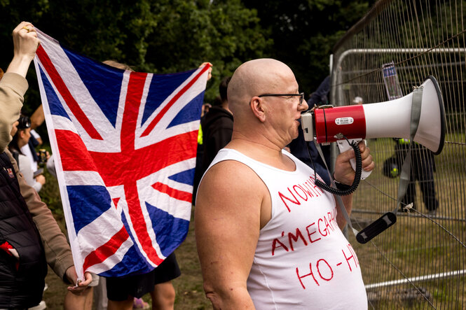 Während ein Demonstrant in ein Megafon spricht, halten andere Protestierende eine britische Flagge hoch