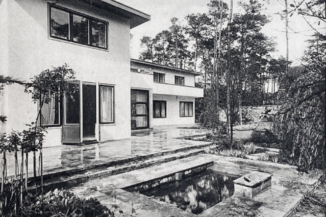 Vor Fenstern und Glastüren erstreckt sich eine Terrasse, davor ein Wasserbecken
