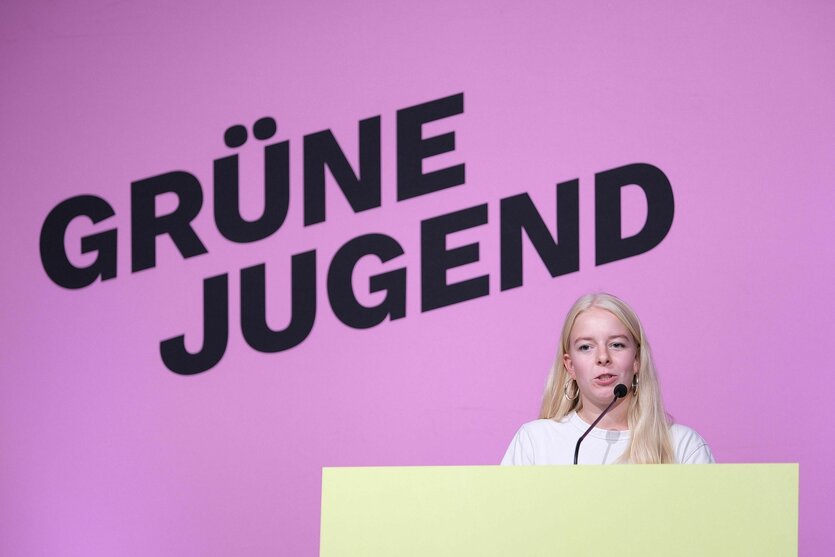 Jette Nietzard steht am Rednerpult, hinter ihr eine Wand in Pink auf der "Grüne Jugend" steht