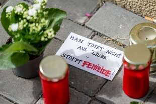 Blumen und Kerzen liegen nach einem tödlichen Messerangriff vor einem Hauseingang in Berlin-Friedrichsfelde neben einem Zettel mit der Aufschrift „Man tötet nicht aus Liebe - Stoppt Femizide“.