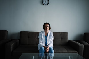 Nina (Ia Suchitaschwili) sitzt in ihrer Klinik im Kittel auf einem Sofa.