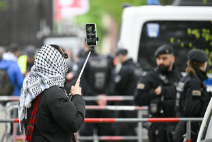 Ein Mensch mit Kufiya filmt Polizisten hinter einer Absperrung
