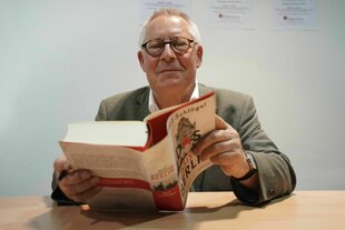 Karl Schlögel, mit Brille und Jacket liest aus seinem Buch und lächelt