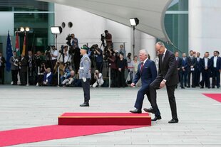 Zwei Männer betreten ein rotes Podest. Dahinter liegt ein roter Teppich