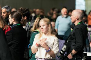 Jette Nietzard steht zwischen Mitgliedern der Grünen auf einem Parteitag und schaut skeptisch
