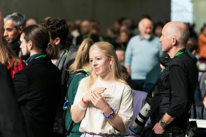 Jette Nietzard steht zwischen Mitgliedern der Grünen auf einem Parteitag und schaut skeptisch