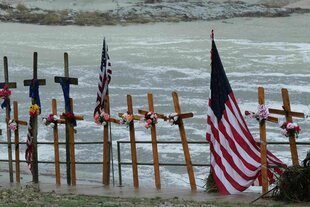Vor dem Hintergrund des Guadalupe River stehen Kreuze und eine US-Flagge