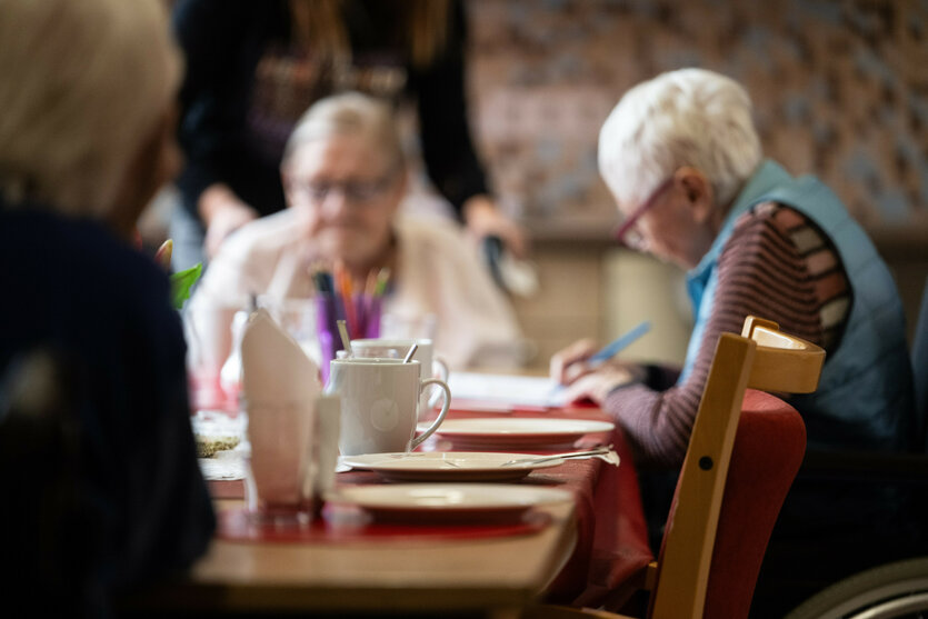 Drei alte Menschen sitzen im Gemeinschaftsraum eines Pflegeheims an einem Tisch