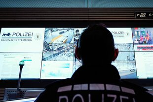 Ein Beamter steht im Führungs- und Lagezentrum des Polizeipräsidiums Mannheim vor einer Wand mit Bildschirmen