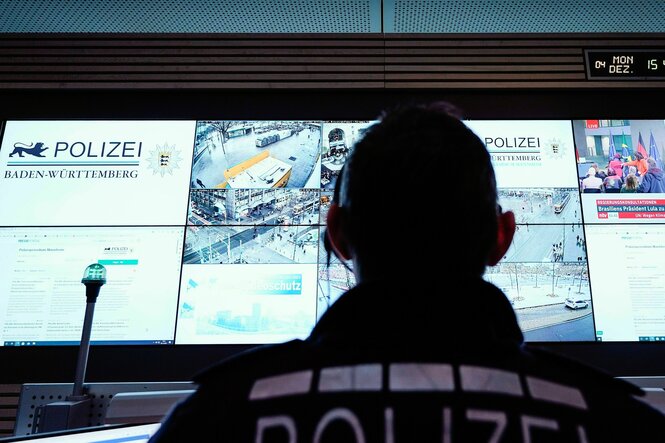 Ein Beamter steht im Führungs- und Lagezentrum des Polizeipräsidiums Mannheim vor einer Wand mit Bildschirmen