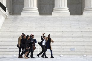 Menschen gehen am Gebäude des Supreme-Courts in Washington vorbei und winken fröhlich