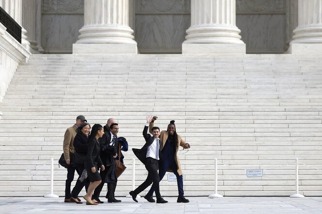 Menschen gehen am Gebäude des Supreme-Courts in Washington vorbei und winken fröhlich