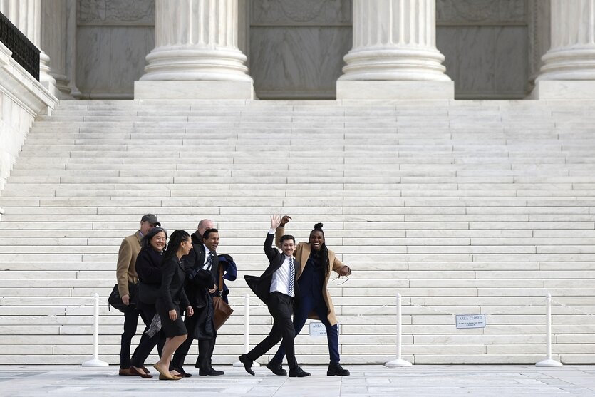 Menschen gehen am Gebäude des Supreme-Courts in Washington vorbei und winken fröhlich