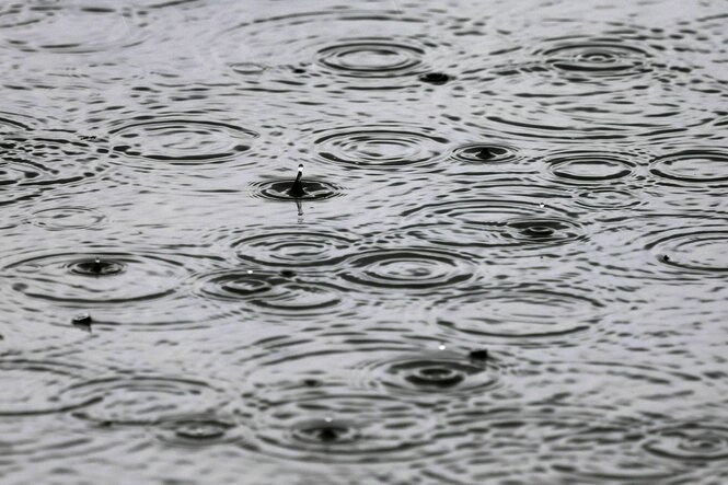 Regentropfen fallen auf eine Wasserfläche