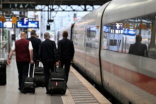 Vier Bahnangestellte gehen an einem ICE vorbei über einen Bahnsteig und ziehen Koffer hinter sich her