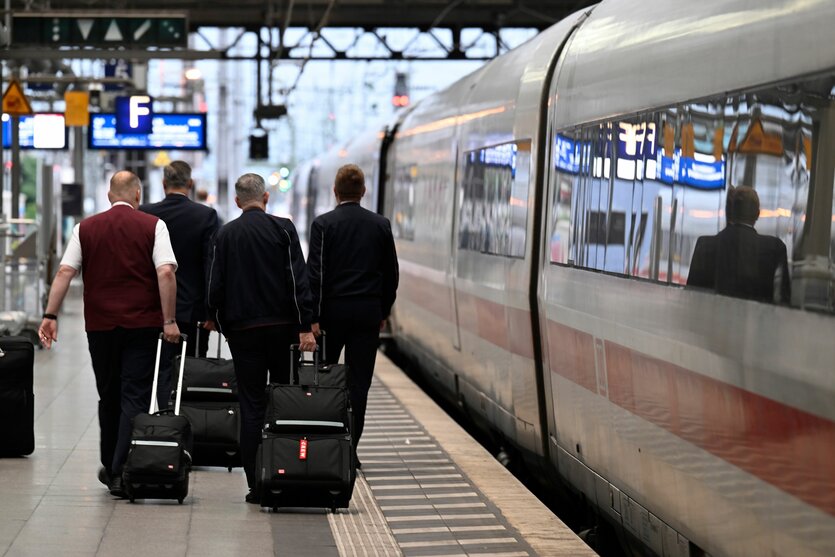 Vier Bahnangestellte gehen an einem ICE vorbei über einen Bahnsteig und ziehen Koffer hinter sich her