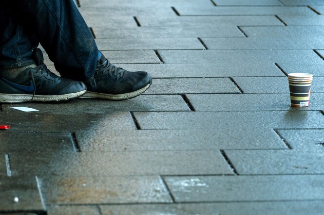 Füße eines Obdachlosen, der einen Becher für Spenden auf das Pflaster gestellt hat