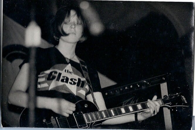 Eine junge Frau mit Gitarre und T-Shirt der Punkband "The Clash"